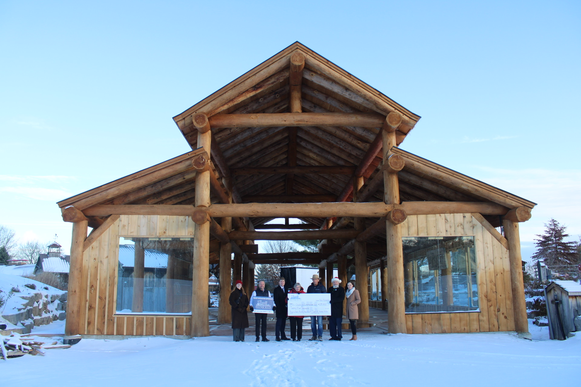 Large barn structure with multiple people standing in front with large cheque